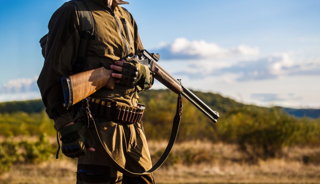 Охотник стоит в поле с разряженным ружьем