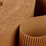 Рулон картону Зображення великих рулонів гофрованого картону, знятих зблизька. Текстура гофрованих шарів картону добре видно, вони створюють цікаві хвилясті форми. Зображення передає деталі структури матеріалу, підкреслюючи його міцність і гнучкість. Тло темне, що контрастує з природним кольором картону.