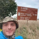 alex На зображенні показаний чоловік у військовій формі та кепці, який зробив селфі на тлі дорожнього знака, що вказує на напрямок до Канева — місця поховання великого Кобзаря, Тараса Шевченка. Напис на знаку дублюється українською та англійською мовами: "Місце поховання великого Кобзаря" та "Burial place of great Kobzar". Чоловік, імовірно, здійснює піший похід і на своєму маршруті проходить через важливі для української історії місця.